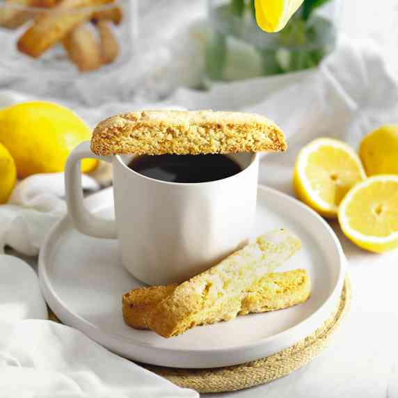 A serving of low carb lemon biscotti on a white plate with a cup of black coffee.