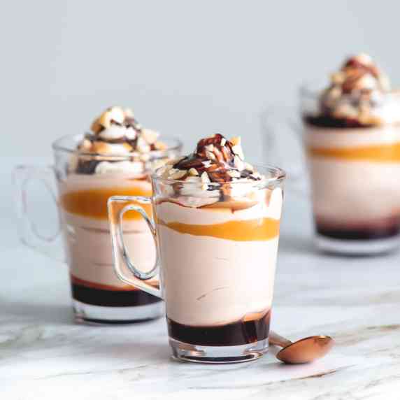 Servings of layered amaretto cheesecake mousse inside a glass on a marble  countertop.