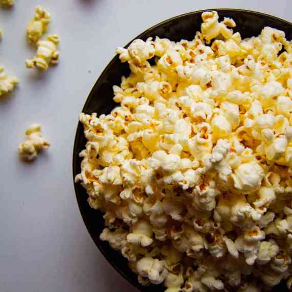 A bowl of buttery, salty homemade popcorn held in hands.