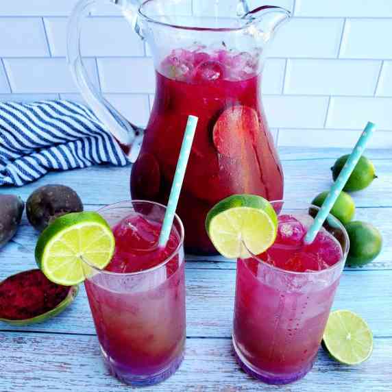 A Pitcher and 2 glasses full of refreshing, prickly pear limeade. Prickly pears, limes around them.