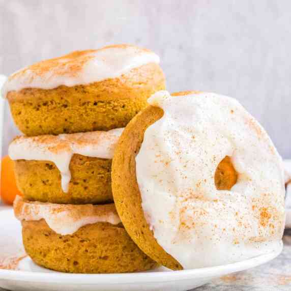 Stack of pumpkin spice donuts each topped with cream cheese glaze.