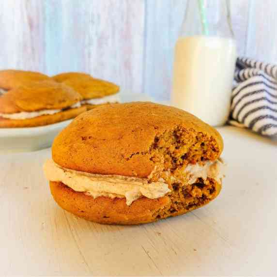 A pumpkin Whoopie pie w/ more in the background & a glass of milk.