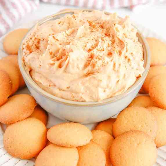 Close up of light orange pumpkin dip on a plate with vanilla cookies.