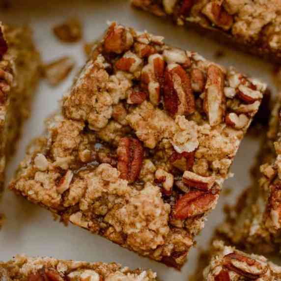 several pumpkin pie pecan bars on a table topped with chopped pecans