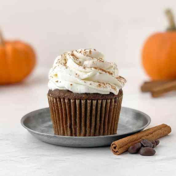 Pumpkin spice latte cupcake on a small metal plate with a cinnamon stick and coffee beans nearby