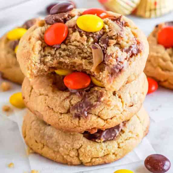 Close up stack of Reese's Pieces topped cookies with the top cookie missing a bite.