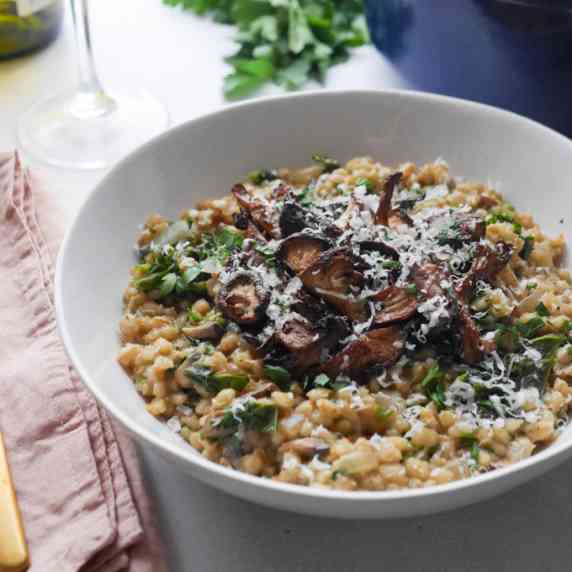 mushroom pearl barley risotto in a white bowl, topped with roasted mushrooms