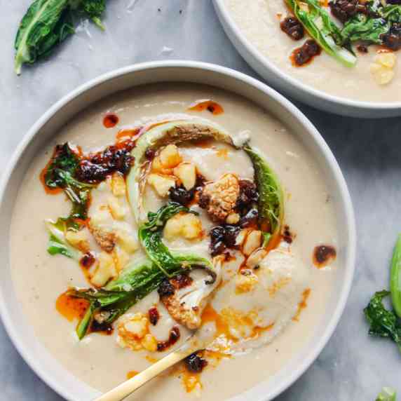 Bowl of creamy cauliflower cheese soup, with crumbled cheese and cauliflower leaves on top.