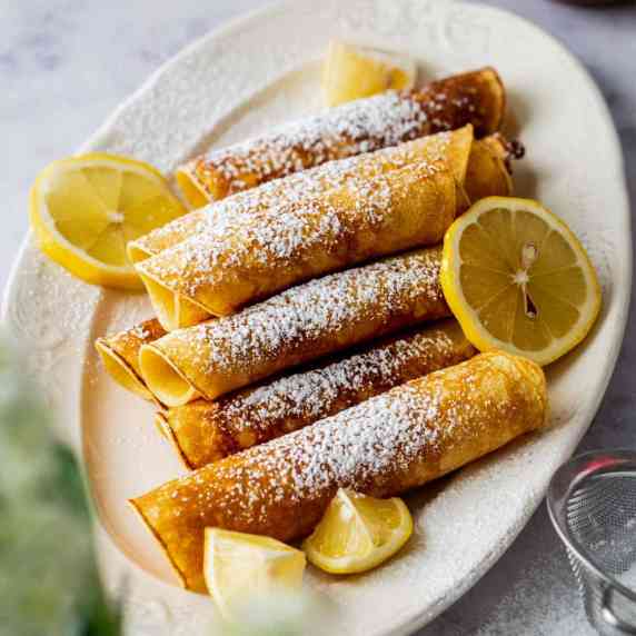 A plate of royal pancakes (they look like crepes) decorated with powdered sugar and lemon slices.