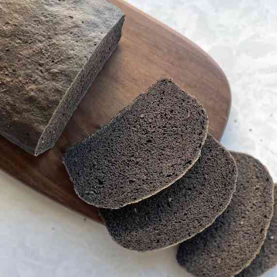 Dark brown slices of bread cut from a loaf of brown bread on a cutting board and grey background.