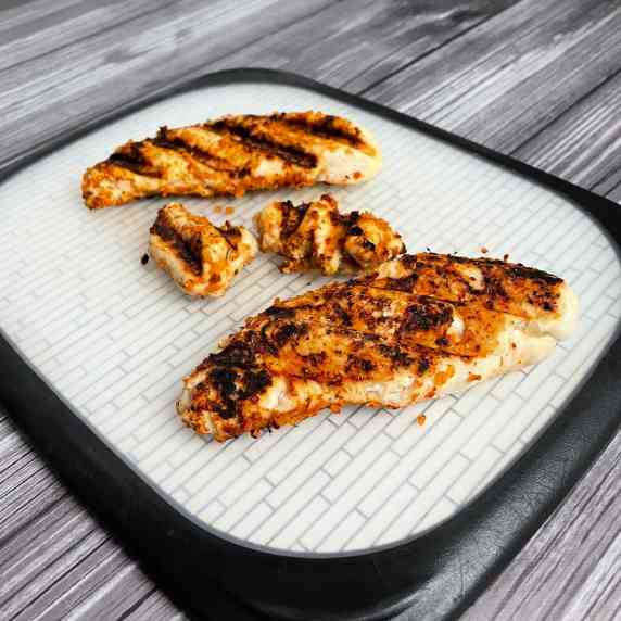 Grilled chicken tenders on a white cutting board