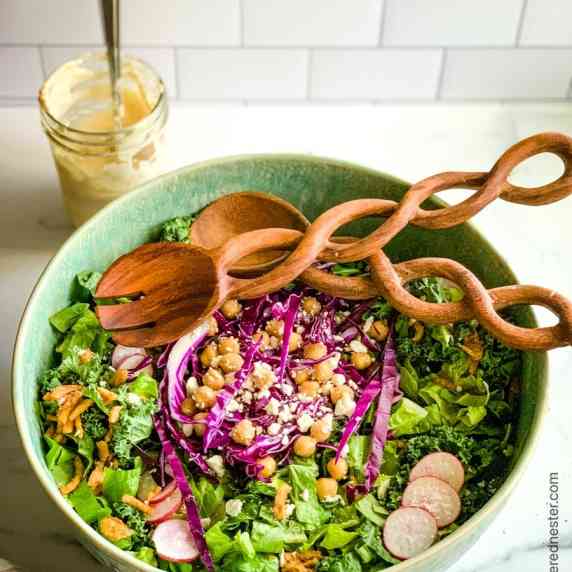 A bowl of kale salad with a wooden serving spoon