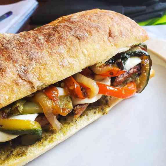 Golden brown toasted ciabatta stuffed with colourful veggies and sausage on a white plate.