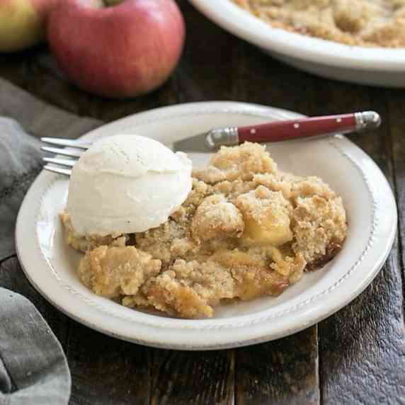Apple crumble on a round white plate with a scoop of ice cream and a red handled fork