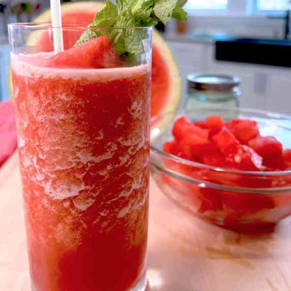 A Watermelon Ginger Mint Slushy in a clear glass with a sprig of mint and a straw
