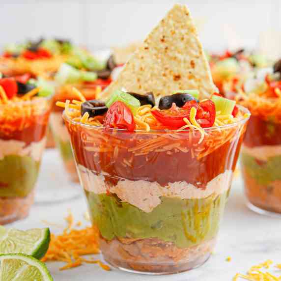 Close view of seven layer dip cups focused in one one cup to see the layers topped with a chip.