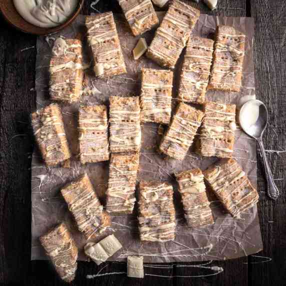 Shortbread fingers drizzled with white chocolate on brown baking paper.