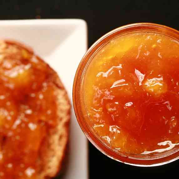 A jar of small batch peach jam next to a piece of toast.