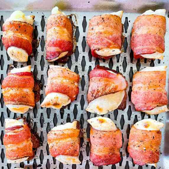 A closeup of smoked bacon-wrapped perogies on a grilling tray.