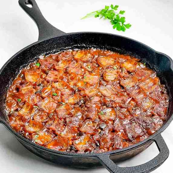 A closeup of smoked baked beans in a cast iron skillet, topped with chunks of bacon.