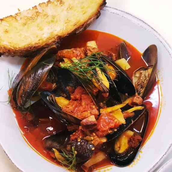 Mussels cooked up in bowl with bread on side.