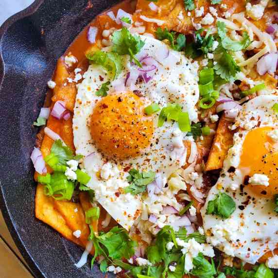 Fried eggs & tortilla chips simmered in red sauce with white feta and pops of green and purple 
