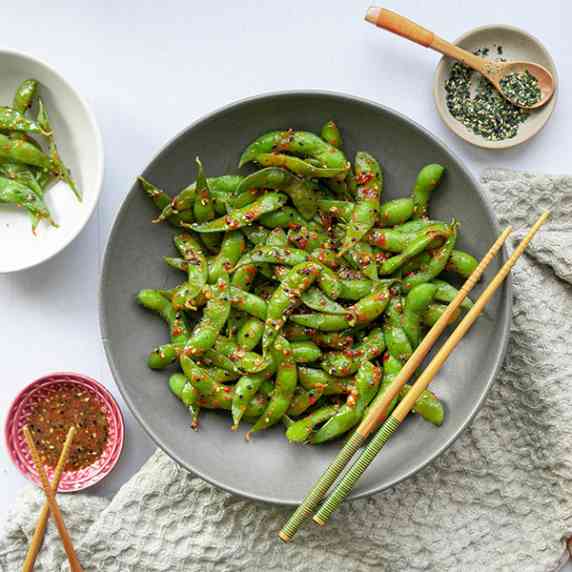 Edamame with spicy sauce in bowl with chopsticks