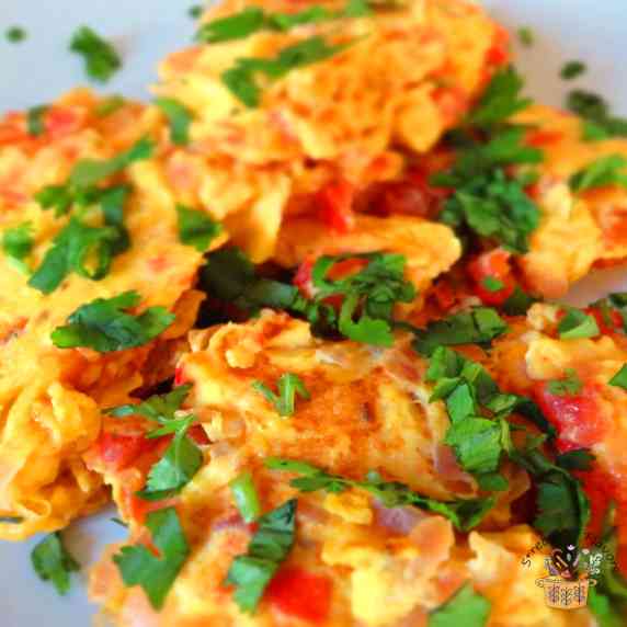 Spicy scrambled eggs with onion and tomatoes garnished with cilantro on a white plate