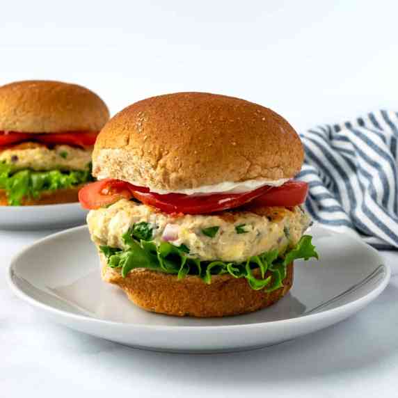 Spinach Feta Chicken Burgers topped with lettuce, tomato and mayo on a white plate.