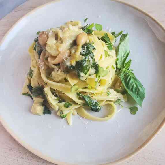 A nest of tagliatelle and greens on a white plate against a wood background.