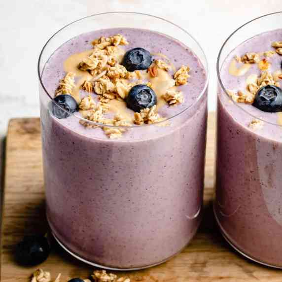 strawberry blueberry smoothies on a wooden board with cashew butter, granola and blueberries on top.