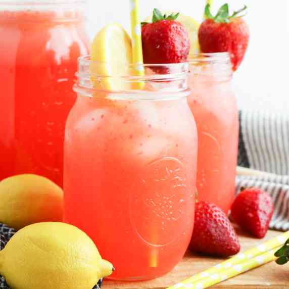 Side view of three glasses of strawberry lemonade topped with fresh fruit.