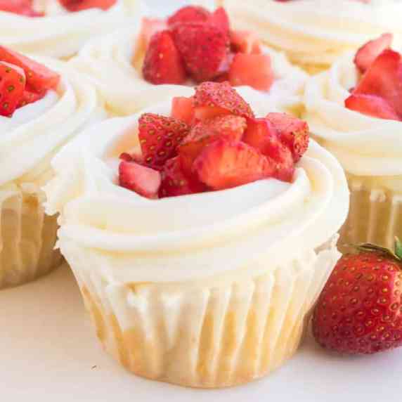 Close-up of a cupcake with frosting and fresh strawberry pieces on top.