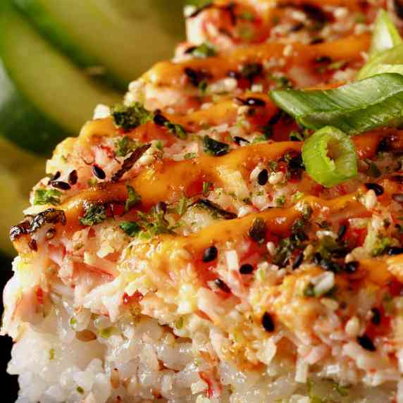 A slice of sushi bake - baked sushi casserole - with cucumbers in the back.