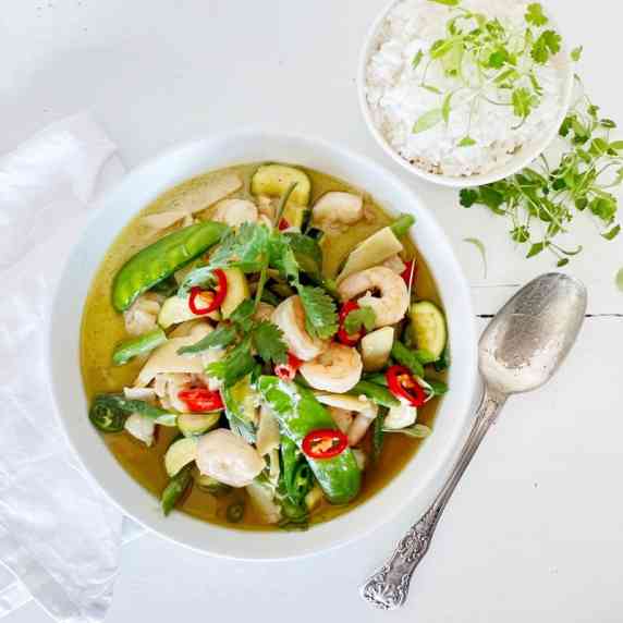 Thai Prawn Green Curry in white bowl on white wooden table top with a small bowl of rice