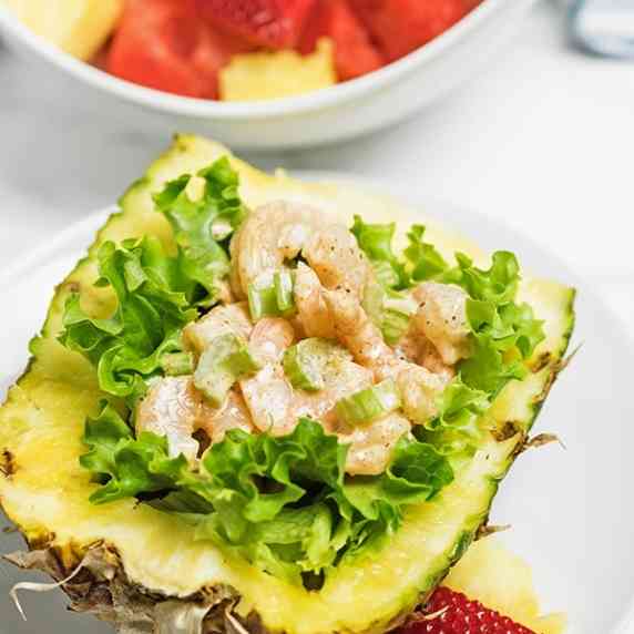 Delicious shrimp salad on a bed of lettuce inside a halved pineapple surrounded by fruit is amazing!