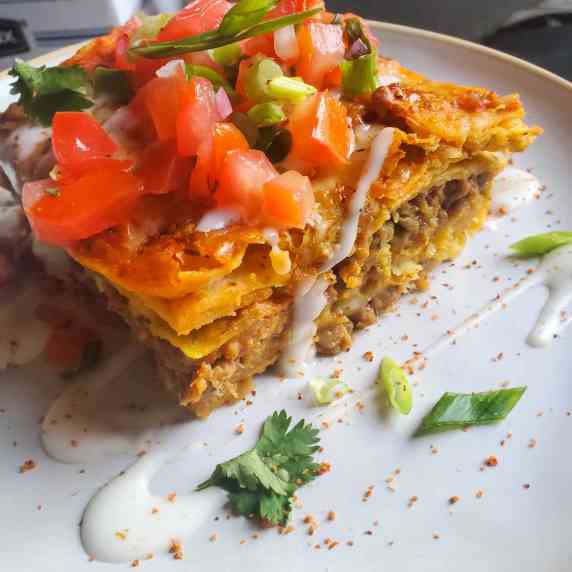 A piece of tortilla casserole on a white plate garnished with green herbs and red Tajin sprinkles.