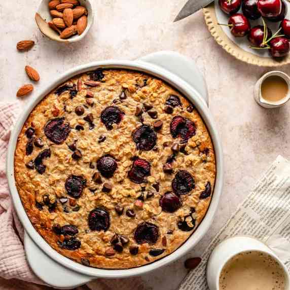 A baking dish of chocolate chip baked oatmeal with cherries to the side with a coffee.