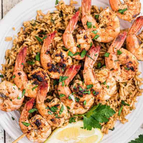 a plate of seasoned rice with some grilled shrimp kabobs sitting on top