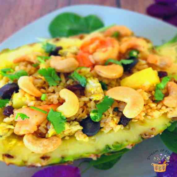 Thai Pineapple Fried Rice in a pineapple half with shrimp, cashews, carrots, raisins, and cilantro