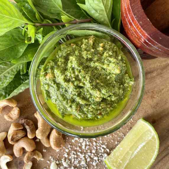 Thai basil pesto in a glass cup with cashews, a lime wedge, salt, and Thai basil around it.