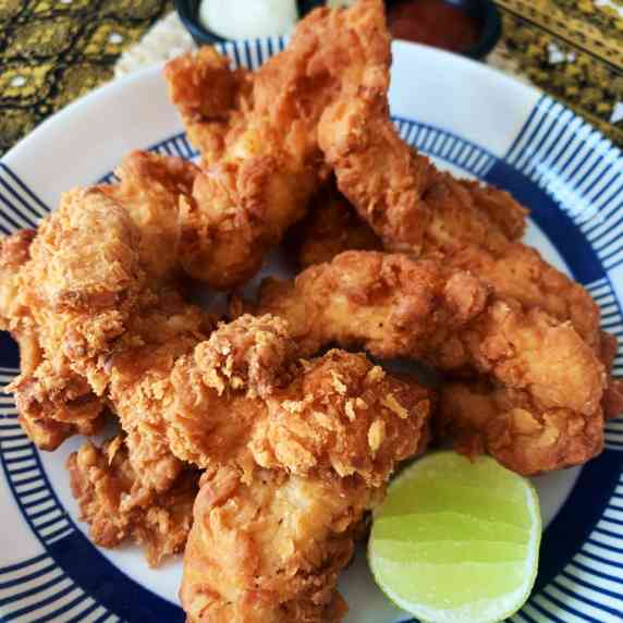 Thai fried chicken tenders in a white dish with a wedge of lime at the bottom.