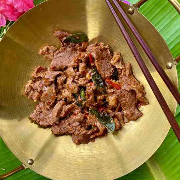 Top-down view of Thai hot and spicy beef stir-fry in a golden dish with chopsticks