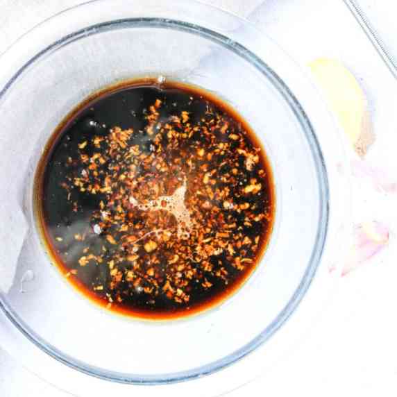 A small glass bowl with soy sauce marinade.