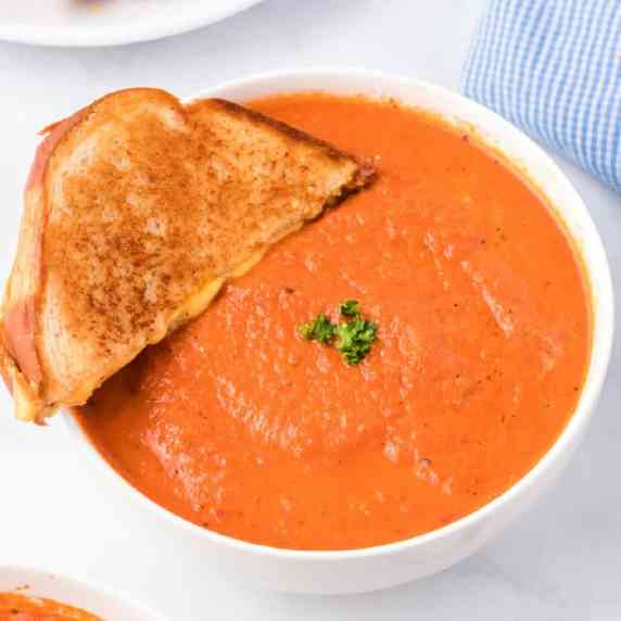 Side view of a bowl of tomato soup with a grilled cheese being dipped into the soup.