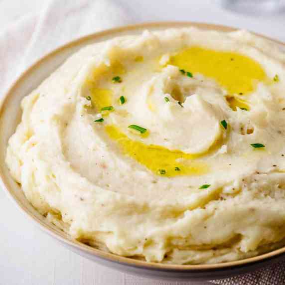 Close up of a bowl of truffle mashed potatoes garnished with olive oil and chopped chives.