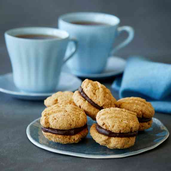 Five vegan and gluten-free kingston biscuits are arranged on a round blue plate. Two blue mugs of te