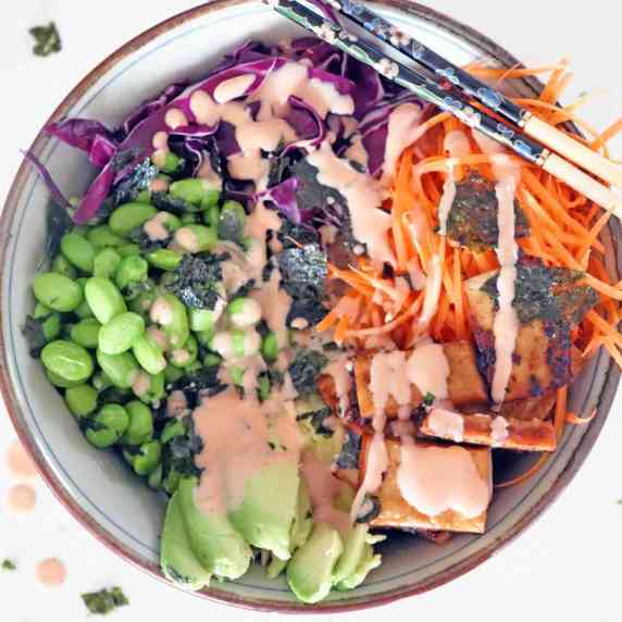 A vegan poke filled with rice, baked tofu, edamame, shredded carrots, red cabbage and avocado
