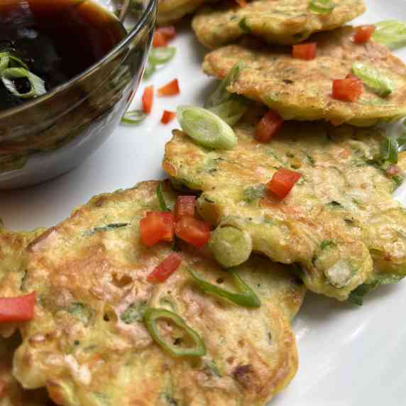 Vegetable pancakes garnished with green onion and red bell pepper, drizzled with gyoza sauce.