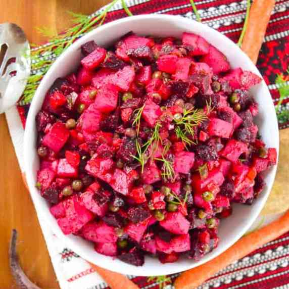 Vinegret in White Bowl with carrots, a beet & serving spoon, on a slavic table runnner